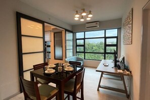 Un coin repas avec une table dressée pour quatre personnes, un canapé et une grande fenêtre donnant sur un paysage verdoyant.