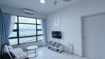 A modern living room with a sofa, a small round table, a TV on a stand, and a large window with curtains.