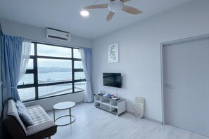 Een moderne woonkamer met een bank, een klein rond tafeltje, een tv op een dressoir en een groot raam met gordijnen.