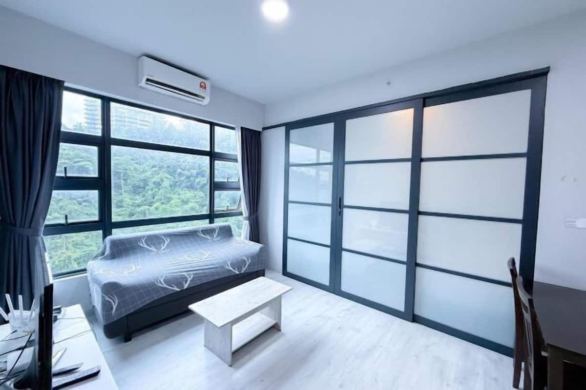 Ein modernes Zimmer mit einem Bett, einem kleinen Tisch und großen Fenstern mit Blick auf Grünflächen.