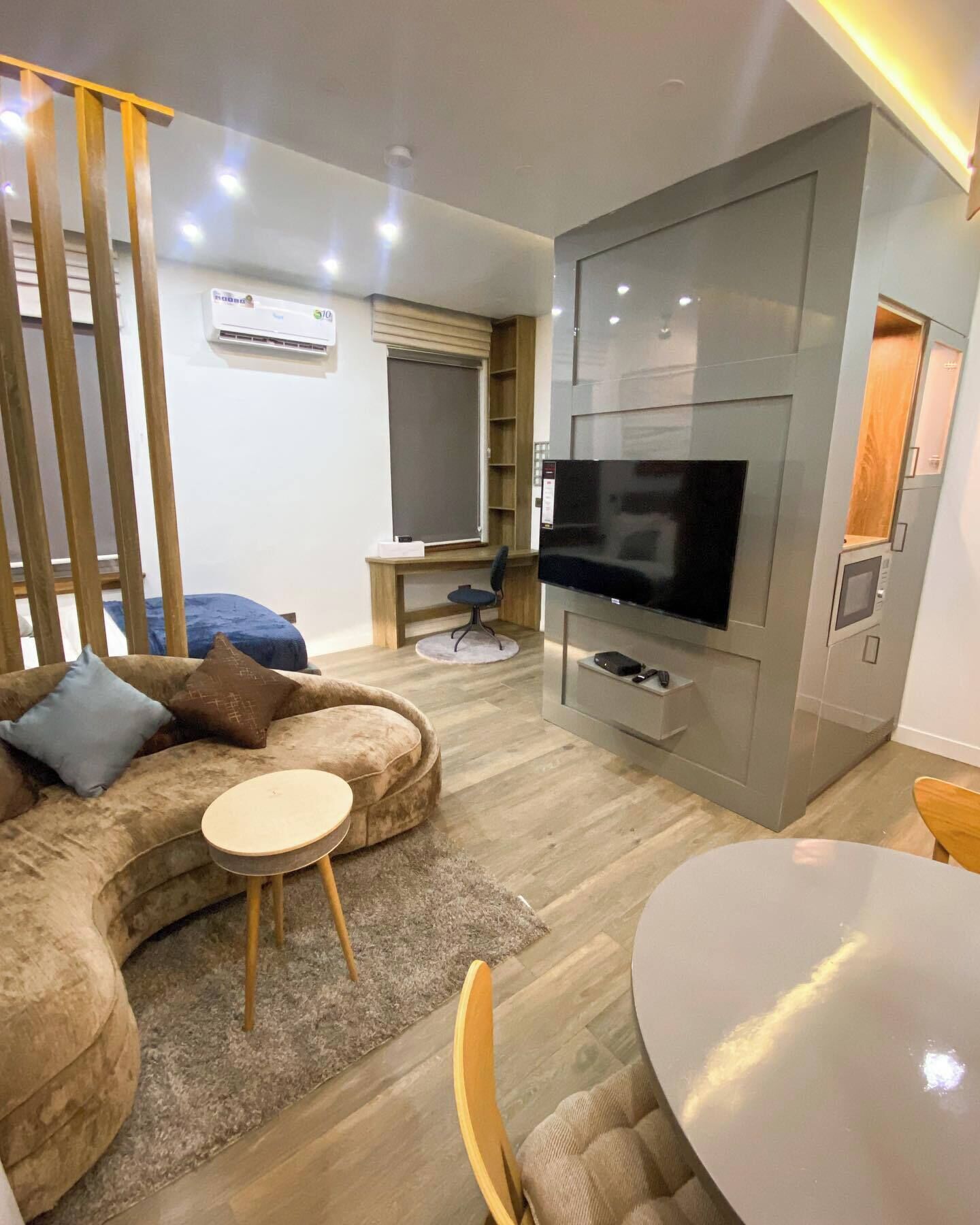 A modern living room with a curved sofa, a small round table, a TV mounted on a grey wall, and a wooden floor.
