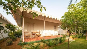 A covered outdoor seating area with a table and chairs, surrounded by greenery and a small garden. - Madho Bagh (Sawai Madhopur)