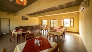 A dining area with wooden tables and chairs, large windows, and hanging pendant lights. - Madho Bagh (Sawai Madhopur)