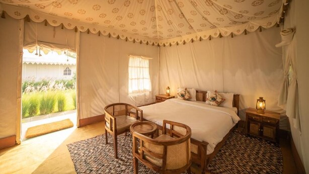 A tent-style room with a bed, two chairs, a small table, and a nightstand with a lamp. - Madho Bagh (Sawai Madhopur)