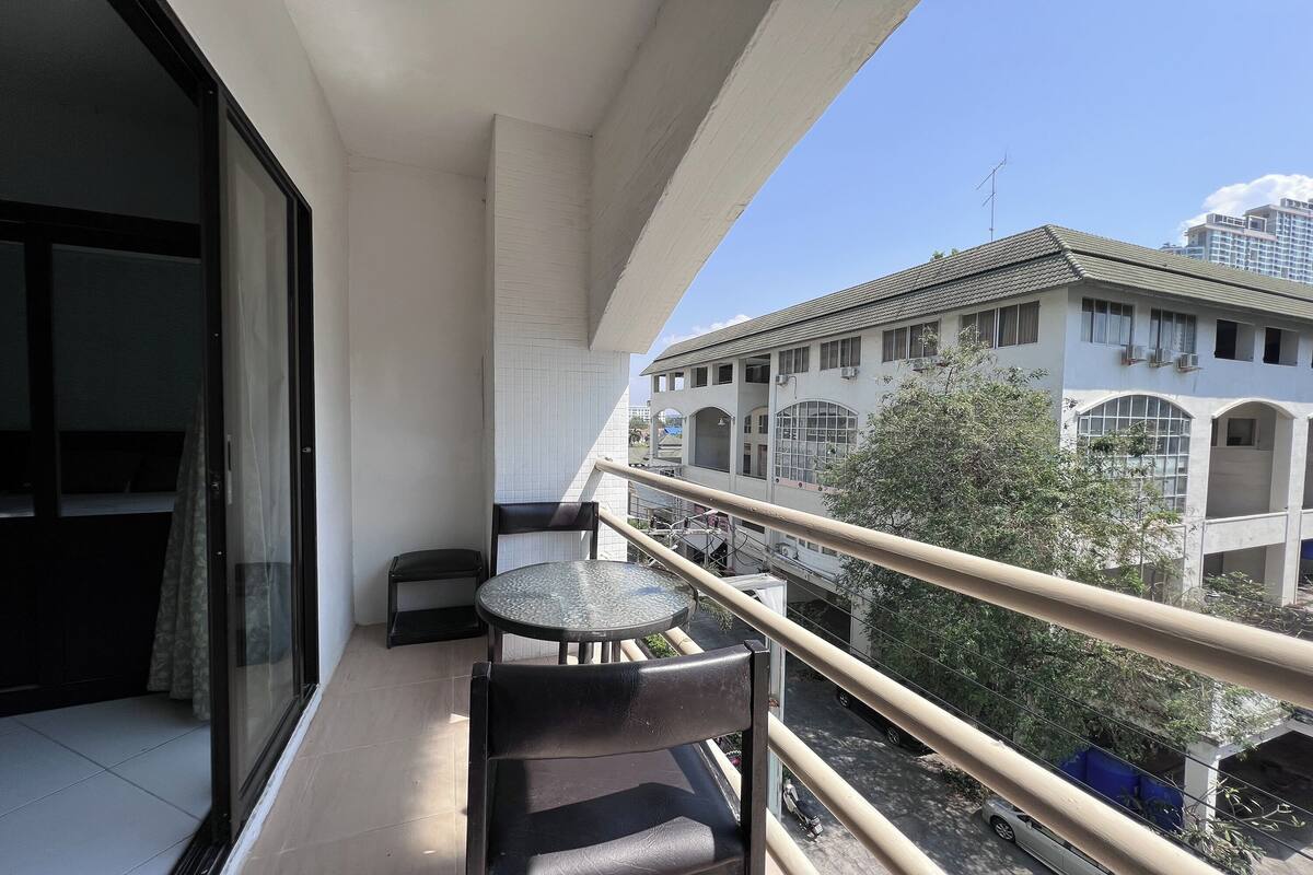 Un balcon avec une table et des chaises, une porte vitrée et une vue sur des immeubles et des arbres.