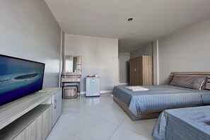 Une chambre d’hôtel avec un téléviseur posé sur un meuble en bois, un lit recouvert d’une courtepointe à rayures bleues, un petit réfrigérateur et une armoire en bois.