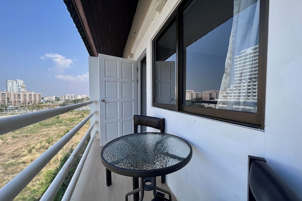 Un balcon avec une table et des chaises en verre, une porte blanche et une vue sur des bâtiments au loin.