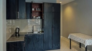 A compact kitchen with dark cabinetry, a small countertop, and a table with a tablecloth. - Emerald Hotel Chonburi (Pattaya)