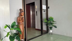 A wooden statue in a hallway with a door, a phone, and a sign. - Emerald Hotel Chonburi (Pattaya)