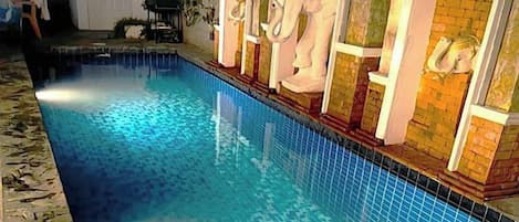 A swimming pool with a tiled edge, a brick wall, and a white door with a decorative handle.