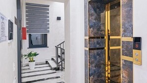 Un interior moderno con una escalera, una planta en maceta y una puerta de ascensor metálica.