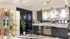 Zona de recepción de un hotel con un mostrador de mármol, una vitrina de cristal con complementos y una planta en maceta.