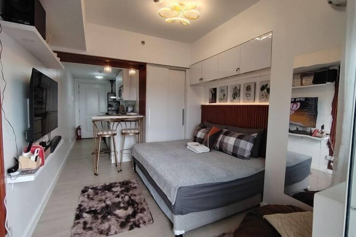 A bedroom with a bed, a desk, a chair, a TV, and a mirror.