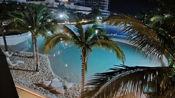 Vista notturna di una zona piscina con palme e un edificio sullo sfondo.