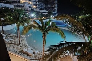 A nighttime view of a pool area with palm trees and a building in the background. - Azure North BLissfully BALI18 (San Fernando)