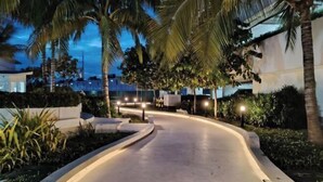 Un percorso curvo fiancheggiato da palme e illuminato da lampioni, che conduce a un edificio dal design moderno.