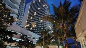 Un hotel moderno con numerosi balconi, palme e un cielo notturno.