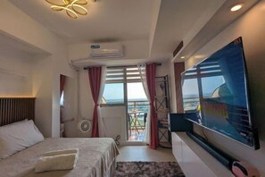 A hotel room with a bed, a flat-screen TV, a balcony with a view, and an air conditioning unit. - Azure North BLissfully BALI18 (San Fernando)