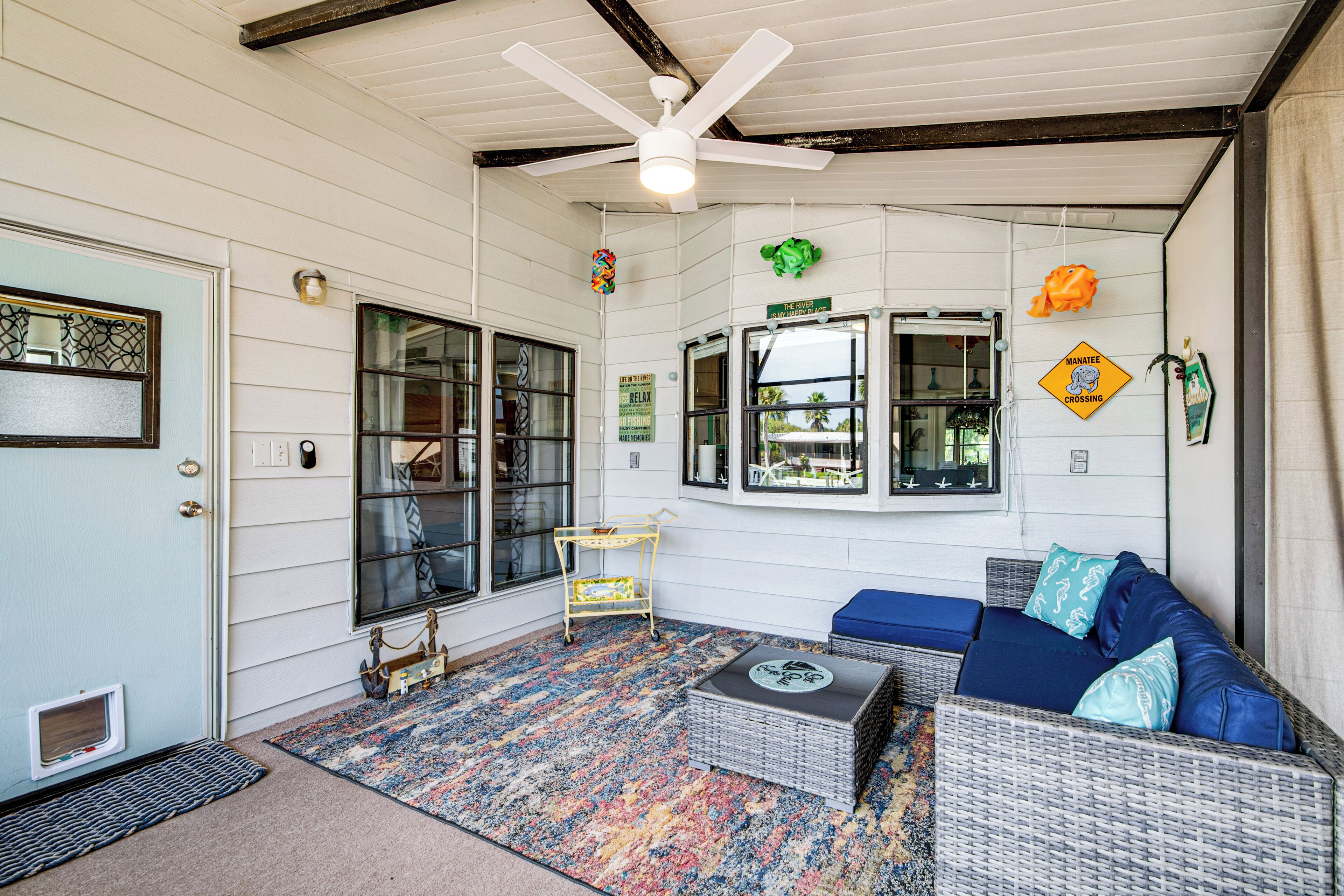 A cozy room with a ceiling fan, a window with a view, a wicker sofa, and a colorful rug.