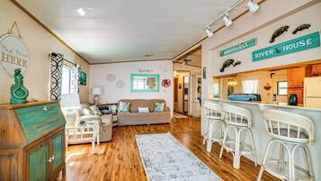 A cozy living room with a wooden floor, a sofa, a coffee table, and a bar area with stools.