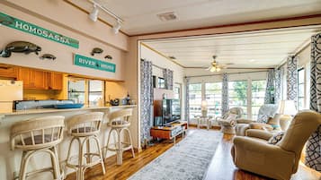 A spacious living area with a kitchen, bar stools, a sofa, and a television.