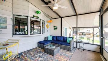 A covered outdoor seating area with a blue sofa, wicker furniture, and a colorful rug.
