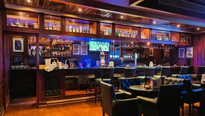 Eine Bar mit Holzböden, gefüllt mit Flaschen, einem Fernsehbildschirm und Ledersitzmöbeln.