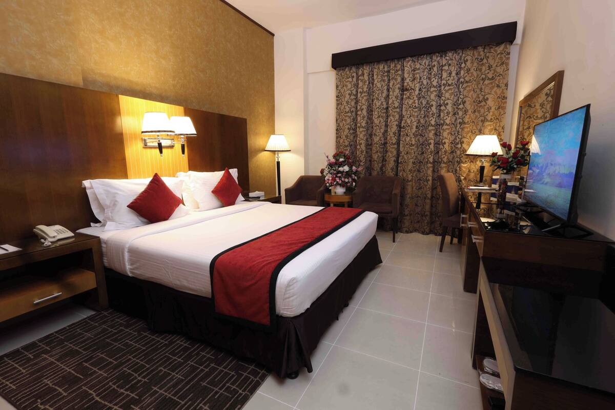 Habitación de hotel con una cama grande, lámparas de noche, un escritorio con televisor y una silla.