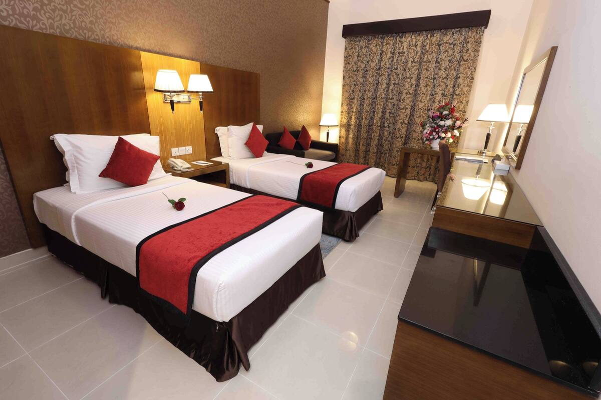 Habitación de hotel con dos camas, una mesita, un espejo y una cortina.