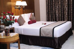 A hotel room with a neatly made bed, a vase of red roses, a lamp, and a telephone on a small table.