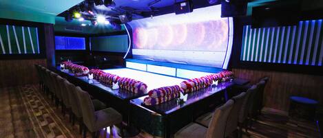 A bar area with a long counter, multiple chairs, and a stage with lighting equipment.