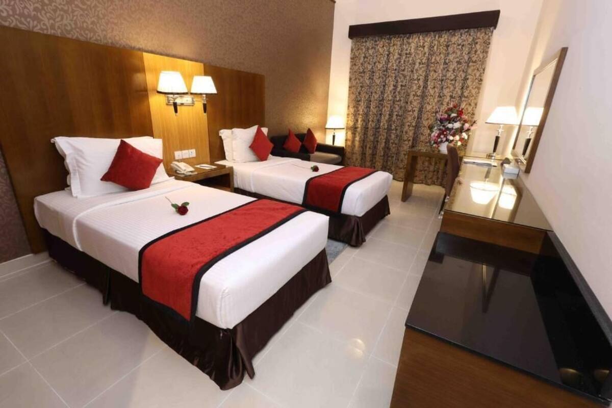 Habitación de hotel con dos camas, un escritorio, un espejo y una ventana con cortinas.