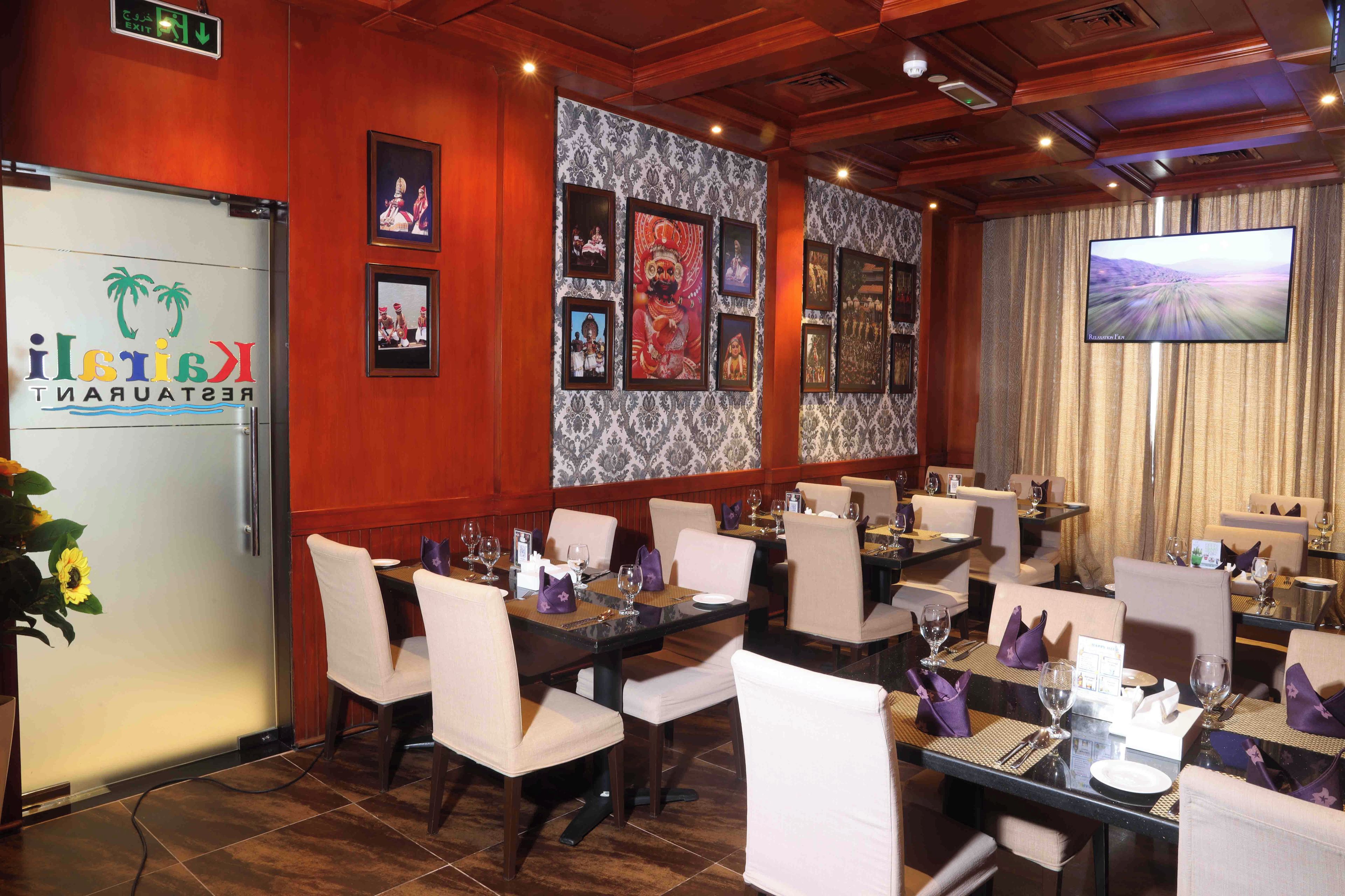 Un restaurante con varias mesas, sillas blancas y una pantalla de televisión grande.
