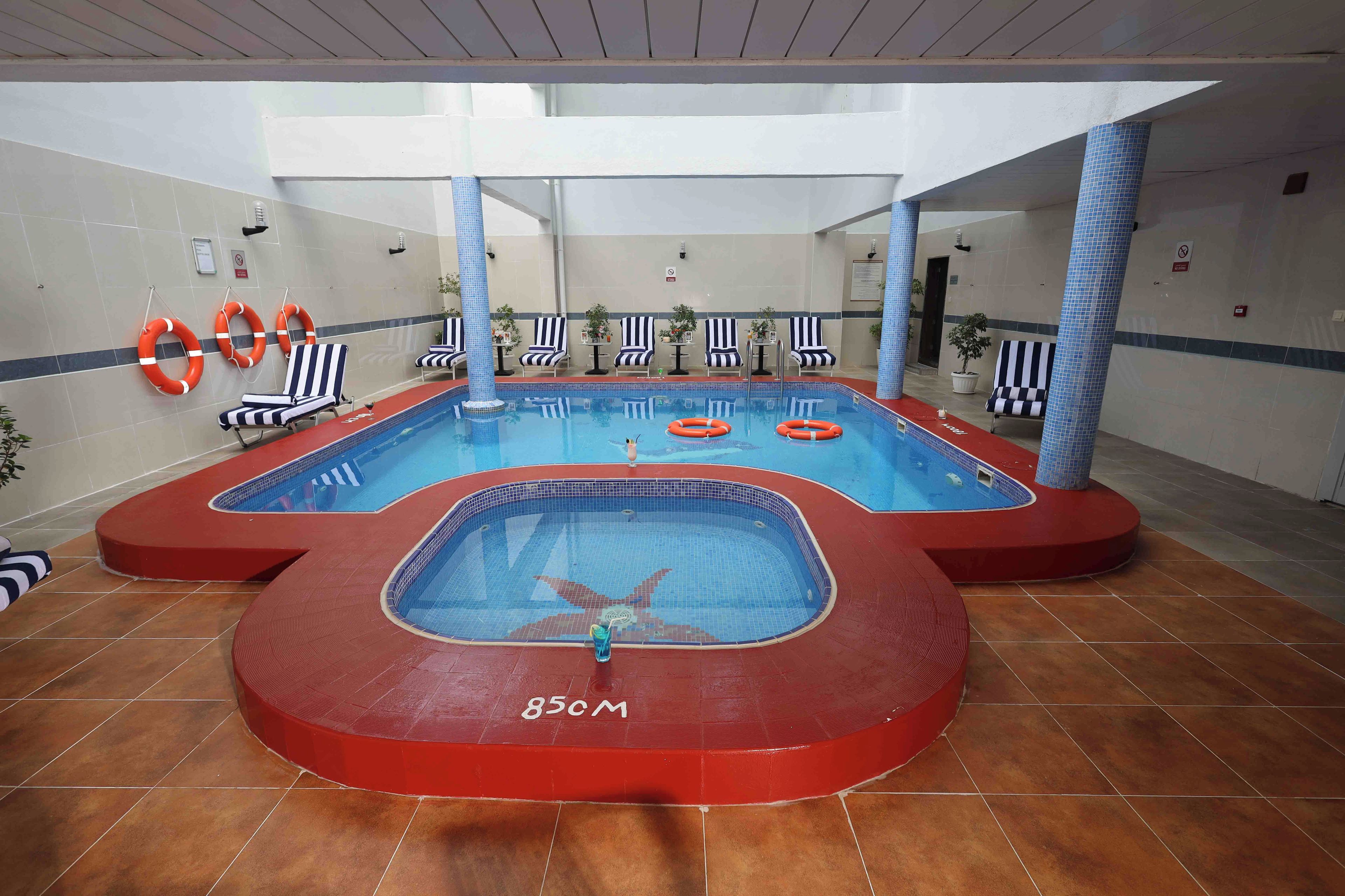 An indoor swimming pool with a red border, lifebuoys, and striped lounge chairs.