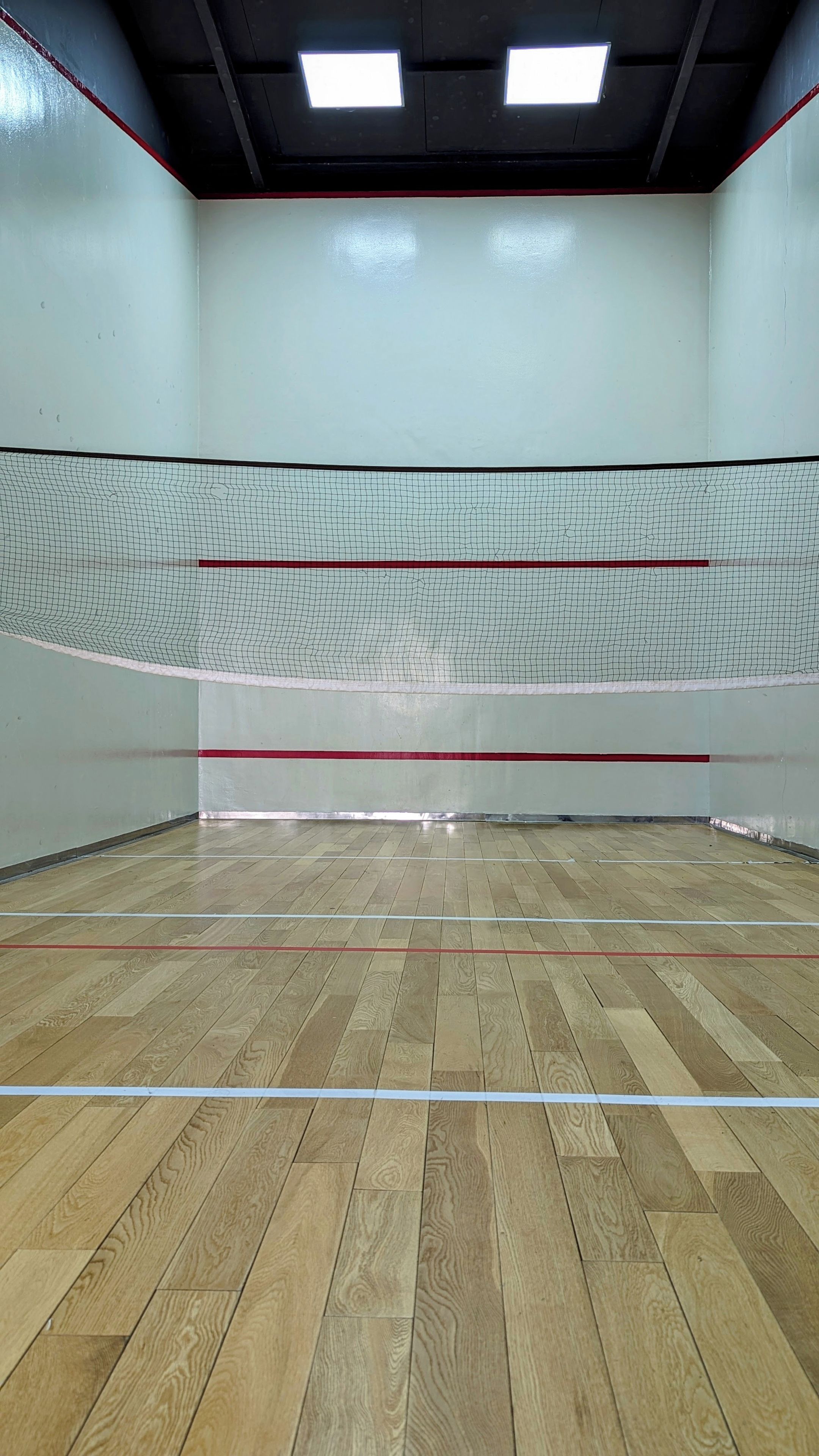 An indoor squash court with a wooden floor, white walls, and a net.