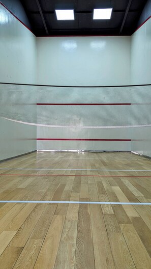 An indoor squash court with a wooden floor, white walls, and a net.