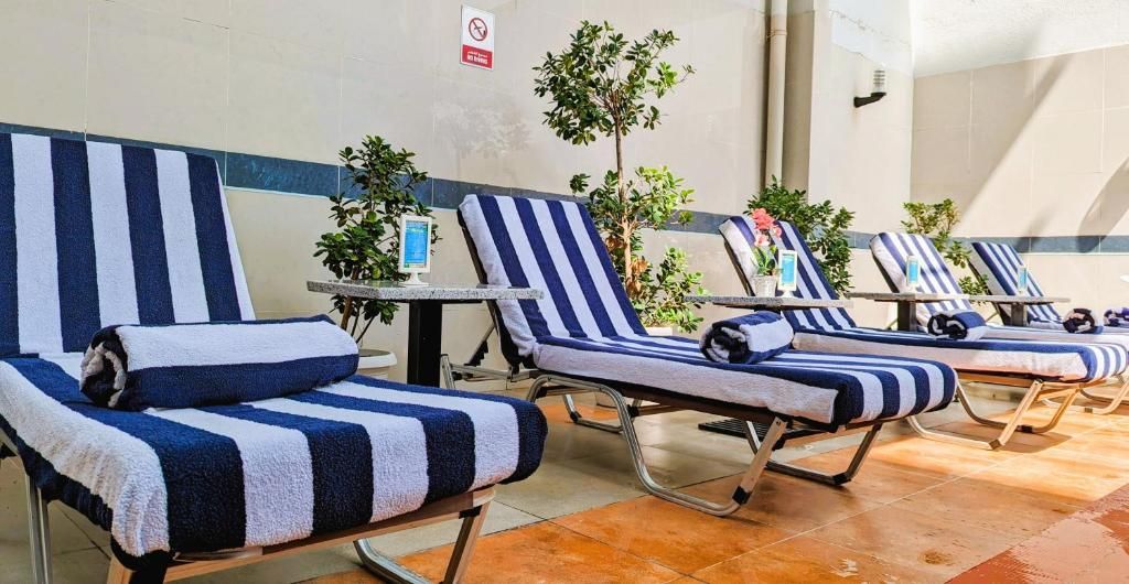 A row of sun loungers with striped towels, a small table, and a plant.