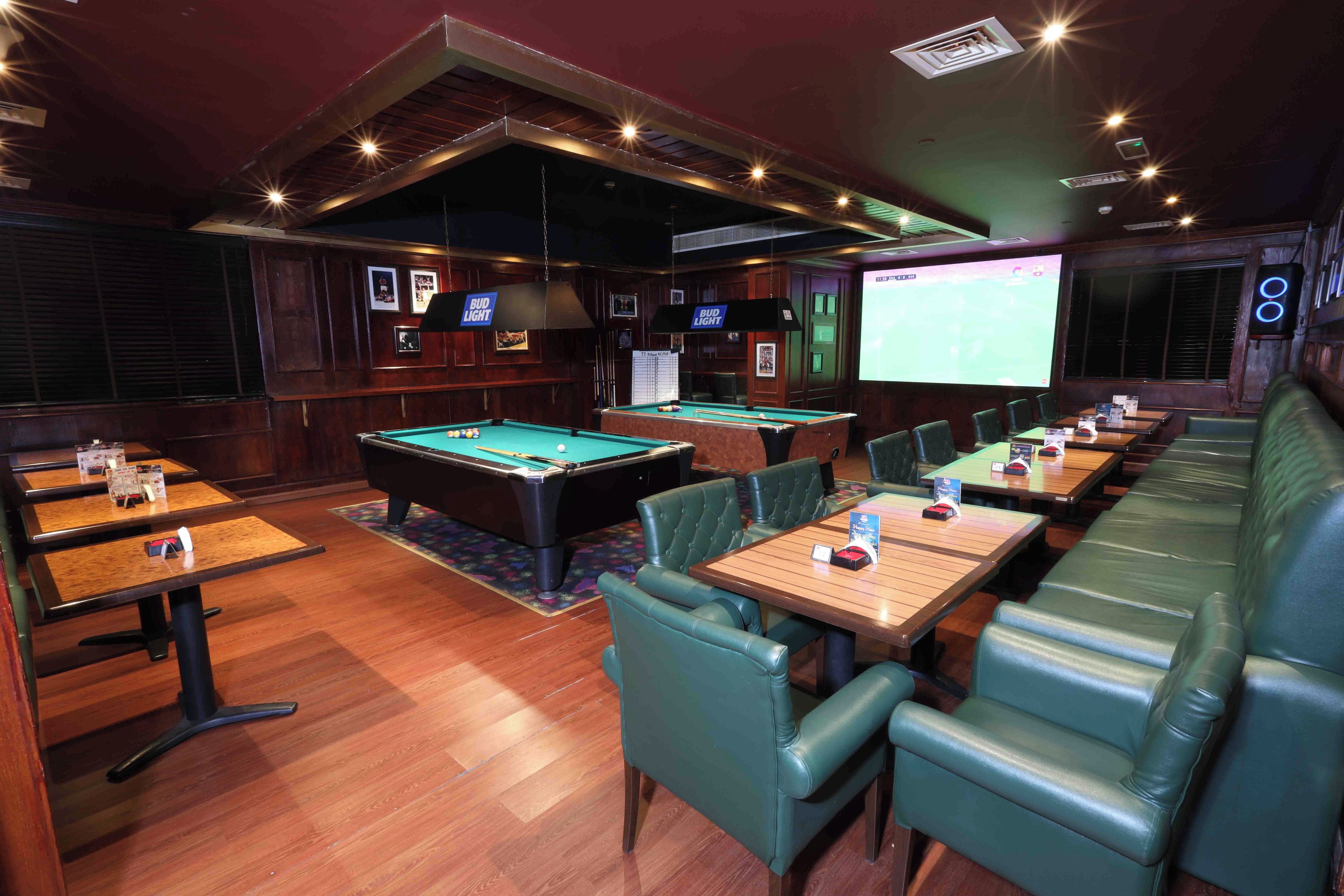 A bar area with pool tables, seating, and a projection screen.