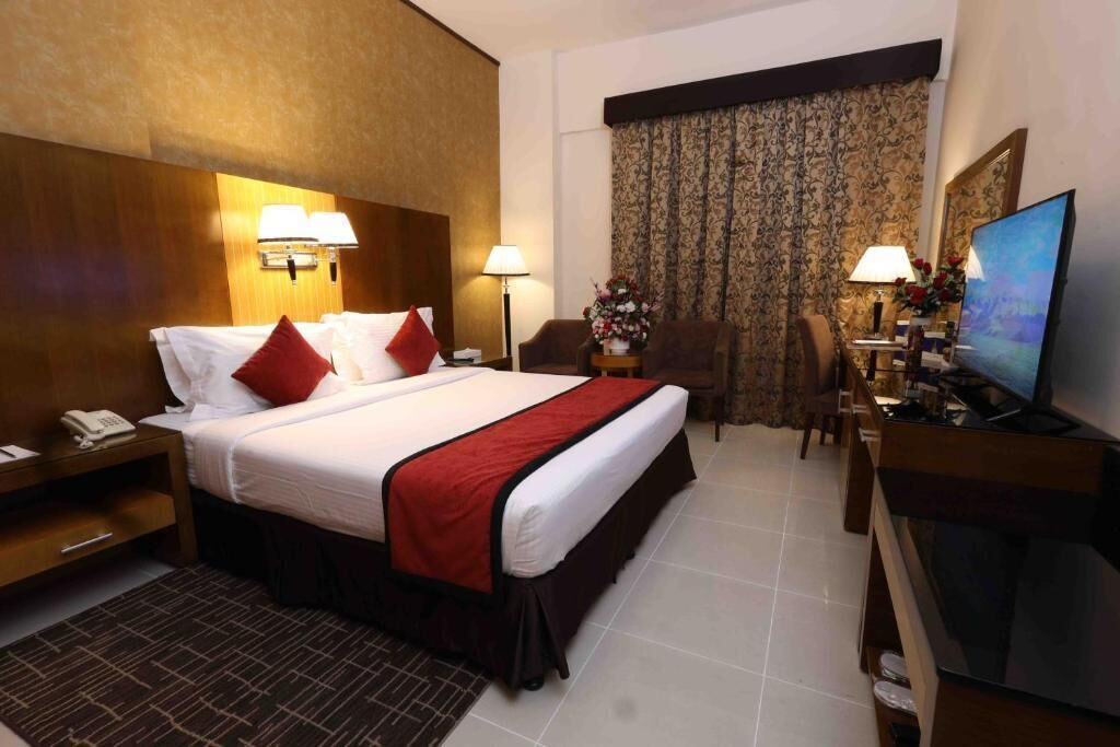 A hotel room with a bed, bedside lamps, a desk with a TV, a chair, and a window with curtains.