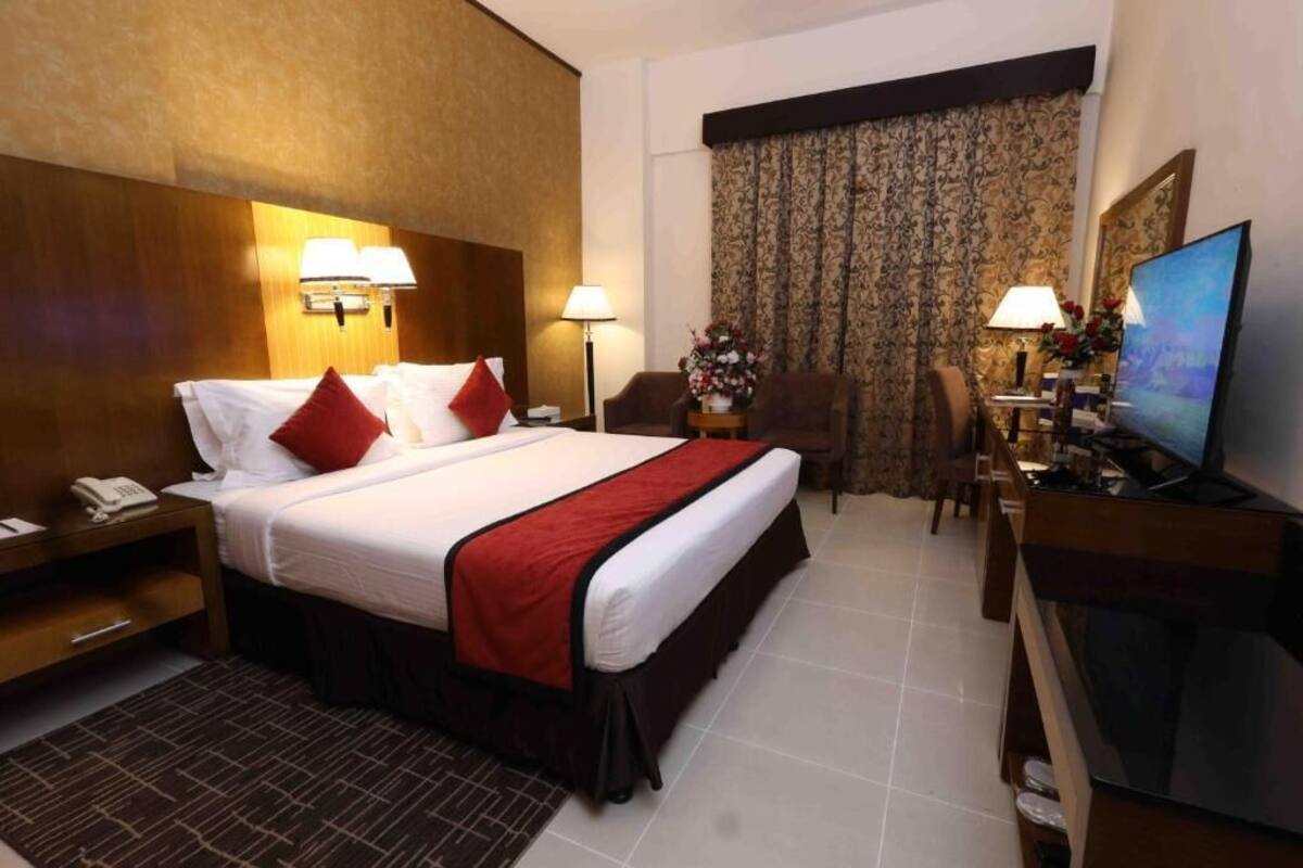 Habitación de hotel con cama, lámparas de noche, escritorio con televisor, silla y ventana con cortinas.