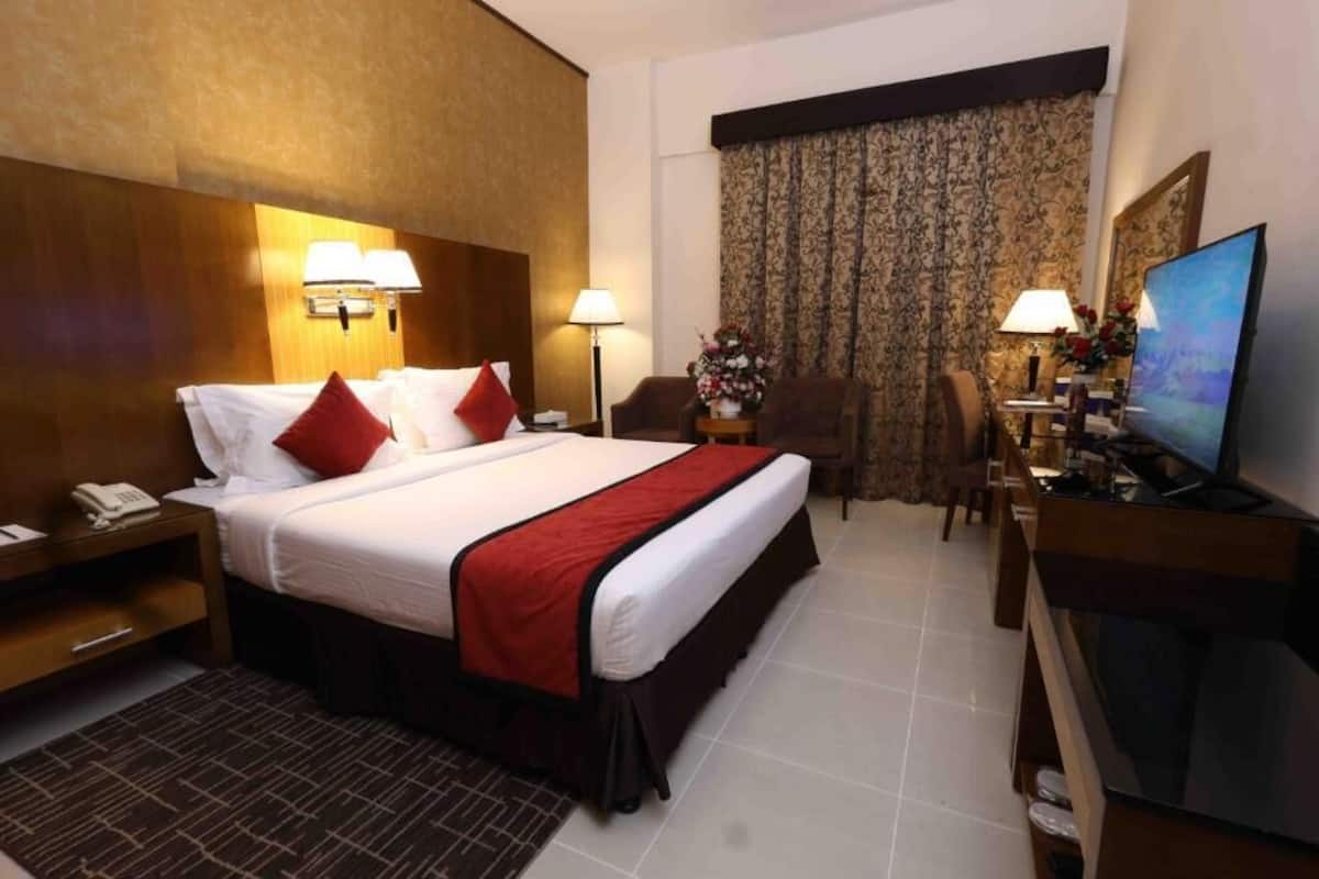 A hotel room with a bed, bedside lamps, a desk with a TV, a chair, and a window with curtains.
