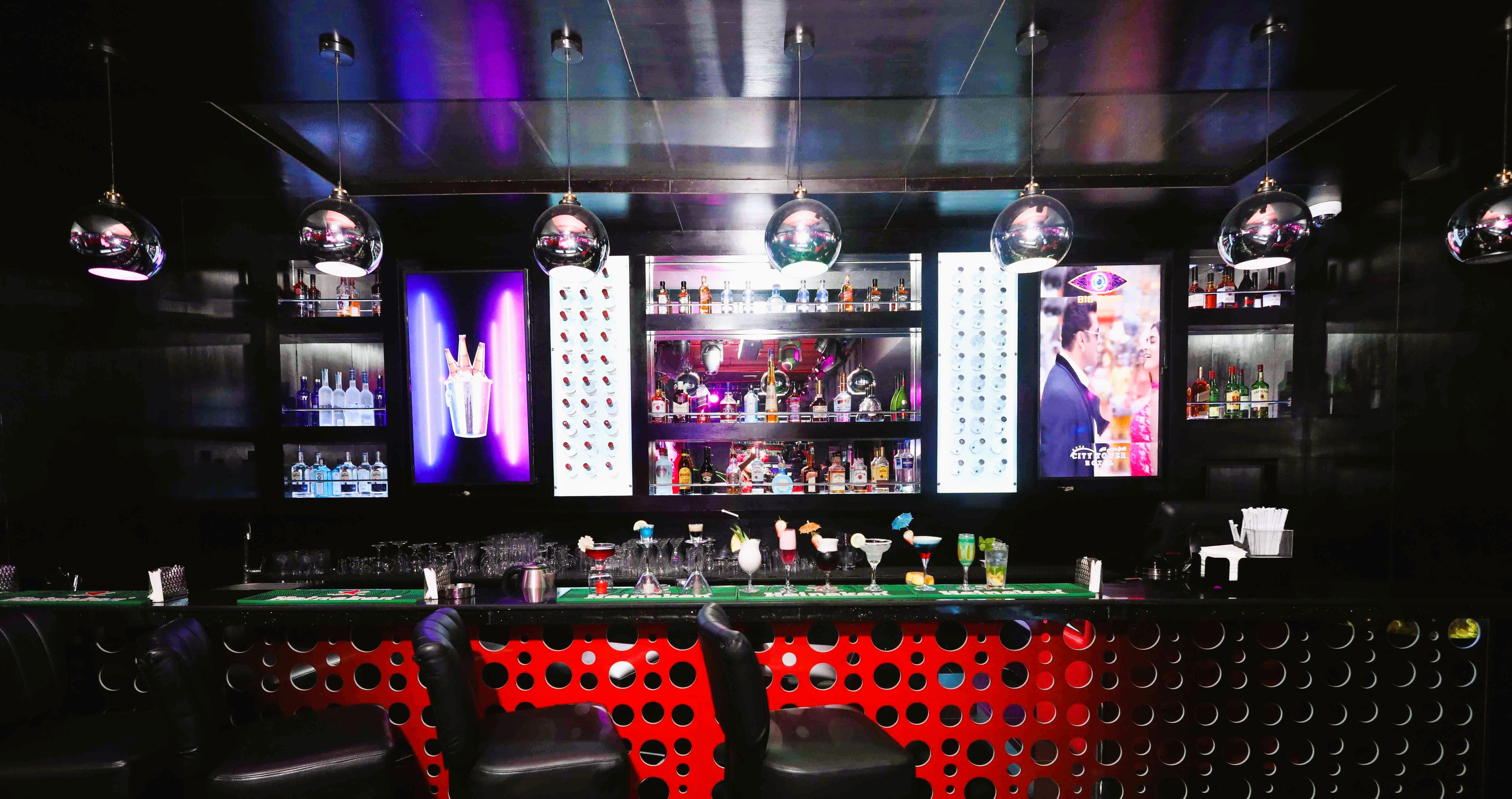 A bar with a red and black patterned counter, shelves with bottles, and hanging disco balls.