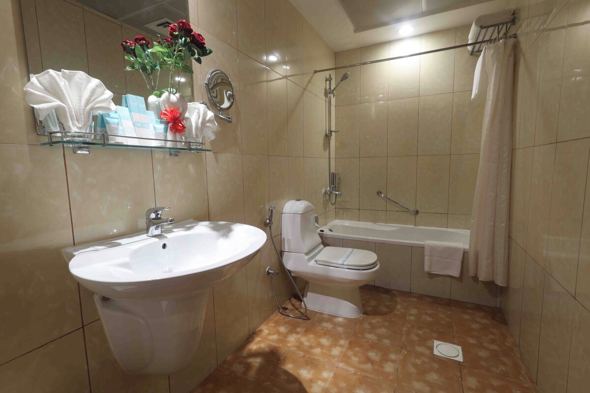 Bagno con lavandino, WC e vasca da bagno. Si nota uno scaffale con articoli da toilette e un vaso con fiori.