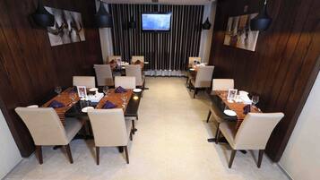 A conference room with two dining tables, chairs, and a TV screen on the wall.