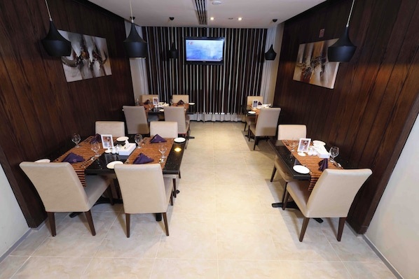 Uma sala de conferência com duas mesas de refeições, cadeiras e uma tela de TV na parede.
