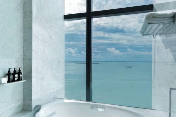 Une salle de bain moderne dotée d’une grande baignoire, d’une douche à parois de verre et offrant une vue sur la mer.