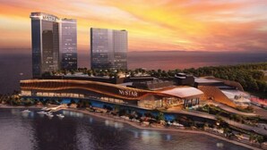 Een hotel aan het water met een modern design, met een opvallend 'NUSTAR' bord, een jachthaven en hoge gebouwen op de achtergrond.