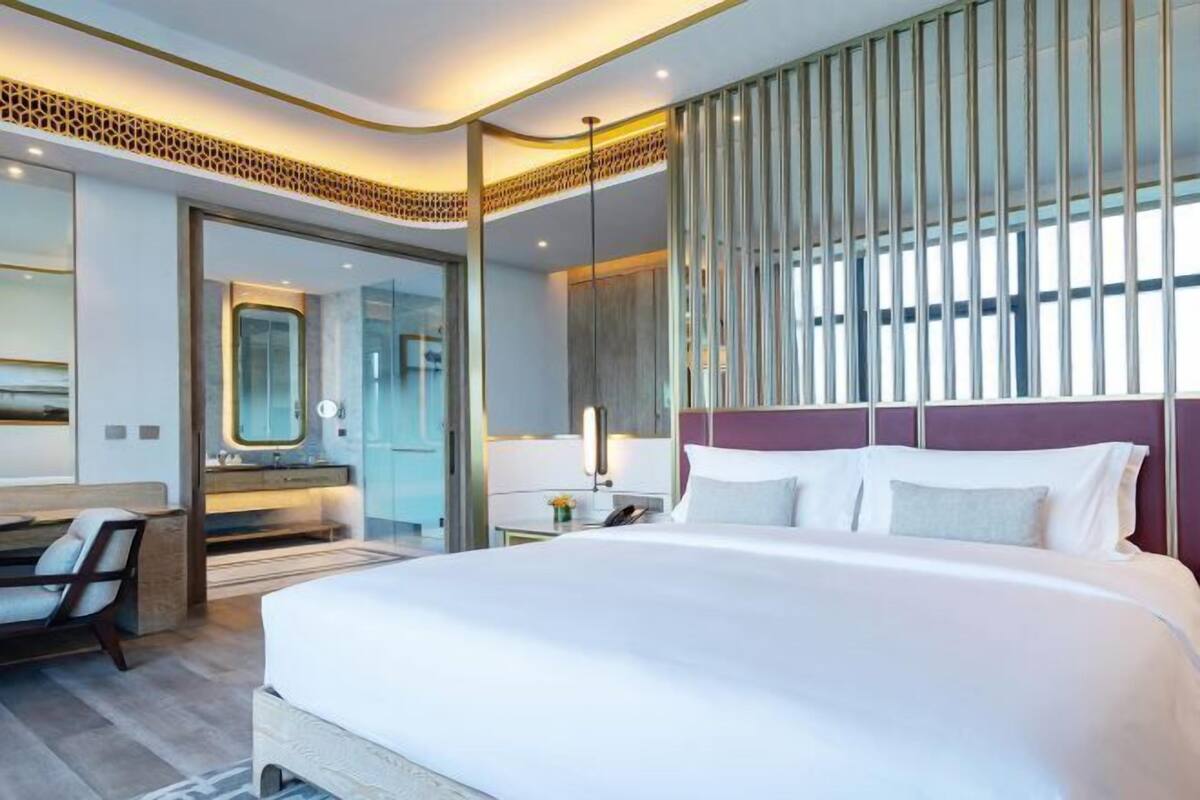 Una habitación de hotel moderna con una cama grande, un escritorio, una silla, un espejo y una ventana con persianas verticales.