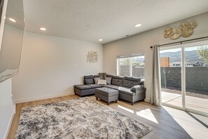 A modern living room with a sectional sofa, a fluffy rug, and a large sliding glass door leading to a patio. - Built in 2025: Parowan Escape w/ Views! (Parowan)