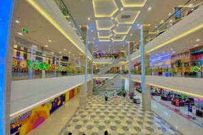 A multi-level shopping mall with escalators, retail stores, and a central open space with a patterned floor.